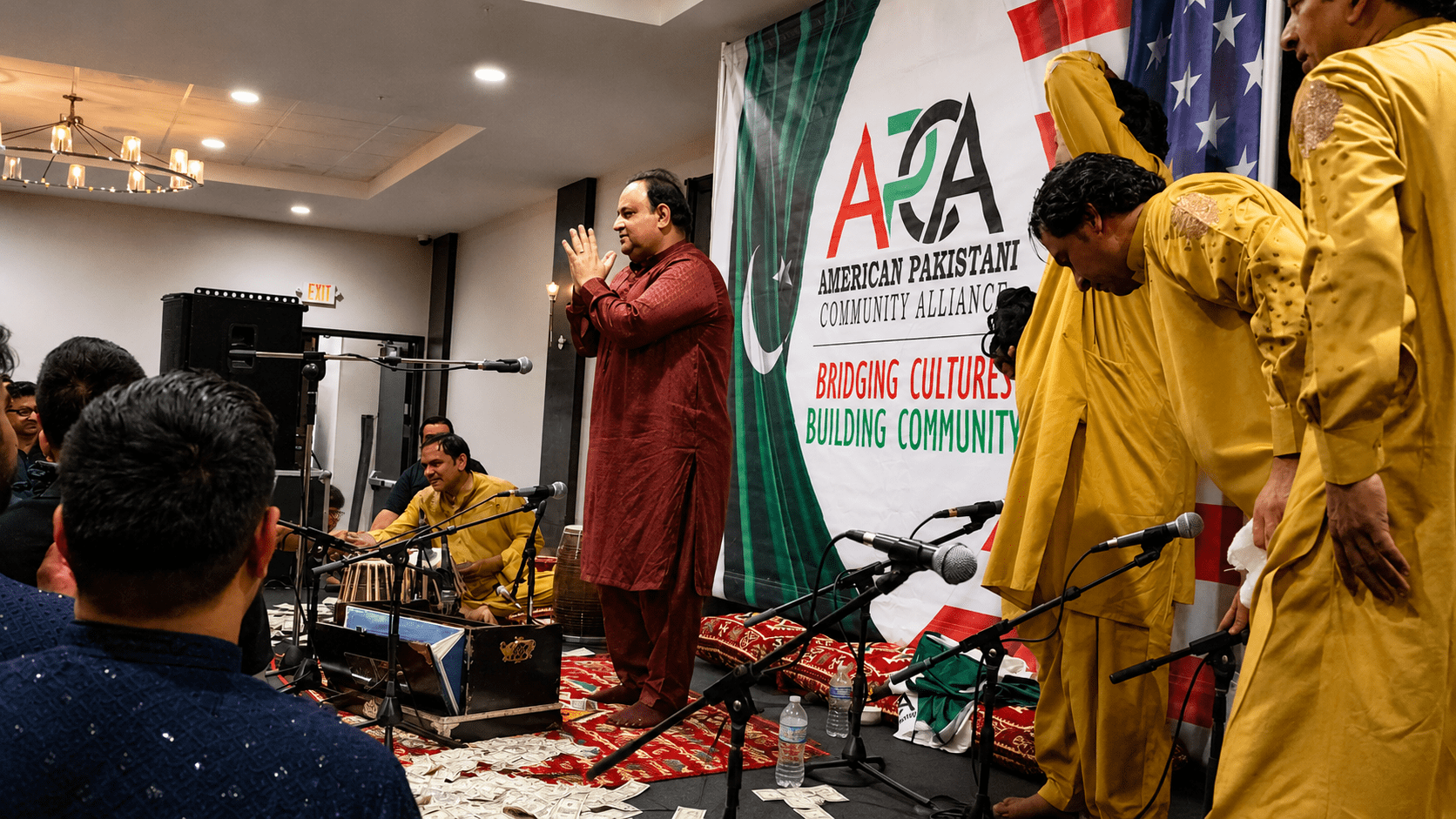 Qawwali performers on stage with APCA banner